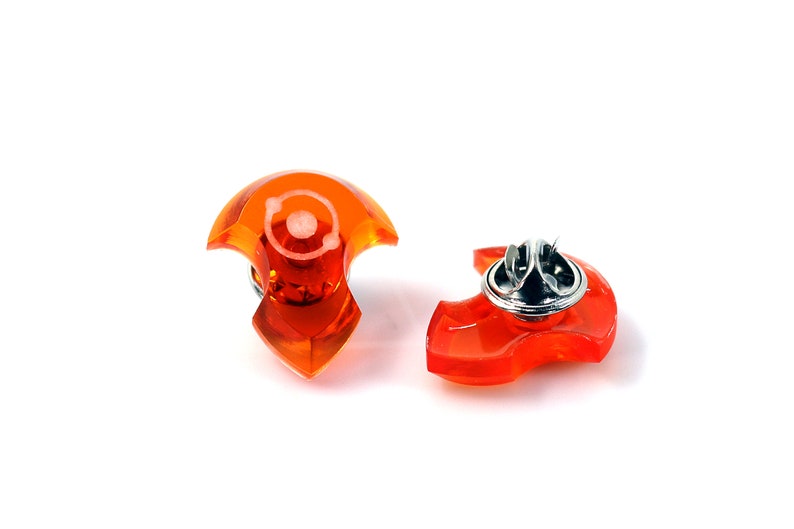 May include: Two orange plastic safety pins with a silver metal pin. The pins are shaped like a crescent moon.