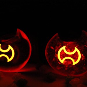 May include: Two red glass orbs with a yellow symbol inside. The symbol is a stylized three-pointed star.