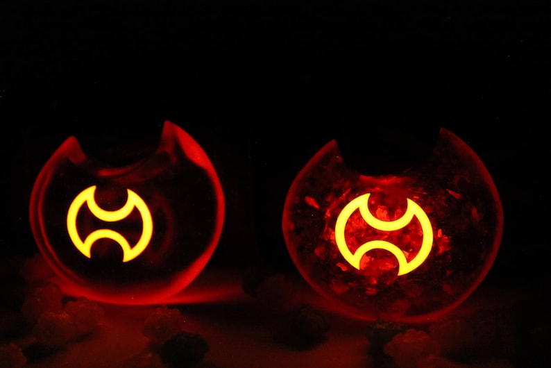 May include: Two red glass orbs with a yellow symbol inside. The symbol is a stylized three-pointed star.