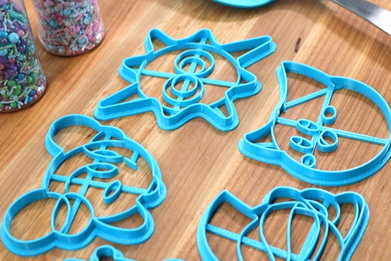 May include: Five blue plastic cookie cutters on a wooden surface. The cutters are shaped like a sun, a cat, a mouse, a bear, and a flower.