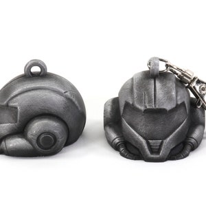 Puede incluir: Dos llaveros de metal de color plateado con forma de casco. Un llavero tiene un anillo de metal plateado.
