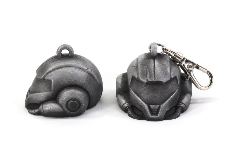 Puede incluir: Dos llaveros de metal de color plateado con forma de casco. Un llavero tiene un anillo de metal plateado.