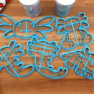 May include: A set of six blue plastic cookie cutters shaped like axolotls. The cutters are on a wooden surface.