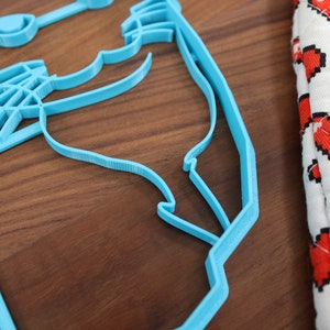 May include: A light blue plastic cookie cutter shaped like a cat's head. The cookie cutter is on a wooden surface.