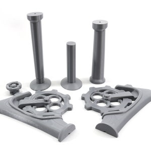 May include: A set of gray 3D printed parts for a steampunk-style mechanical device. The set includes two tall columns, a shorter column, two gear-shaped bases, and a small knob.