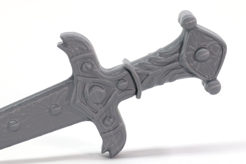 May include: A gray plastic sword with a detailed handle and a sharp point. The handle has a decorative design with a raised center piece.