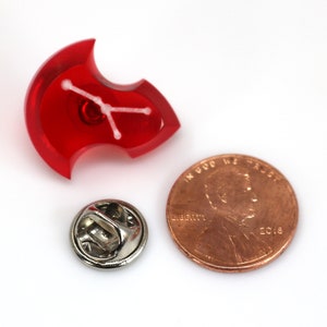 May include: Red plastic pin with a white constellation design. The pin is about the size of a US penny.