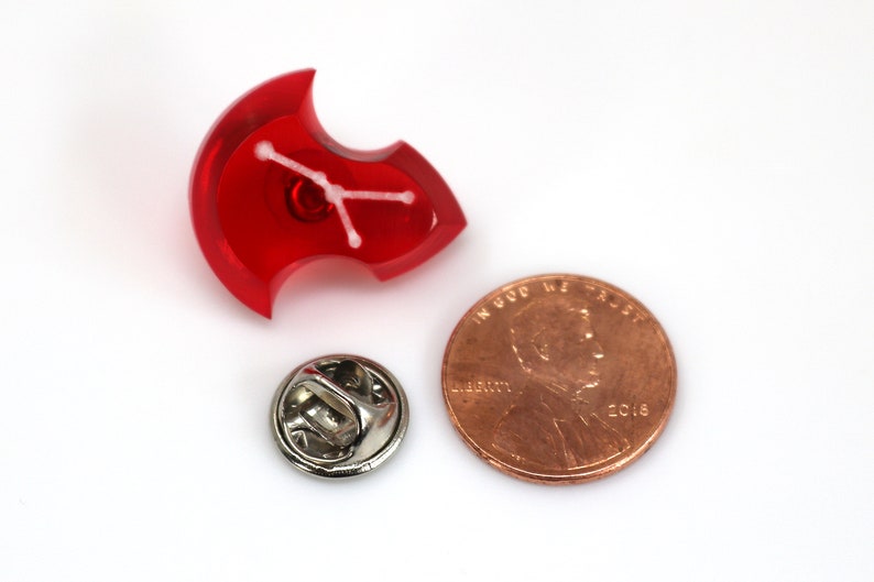 May include: Red plastic pin with a white constellation design. The pin is about the size of a US penny.