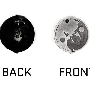 May include: A silver-colored metal charm with a yin yang design featuring two cats facing each other. The back of the charm is plain and black.