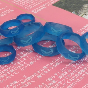 May include: A group of seven translucent blue rings with a geometric design. Each ring has a white design on the inside of the ring.