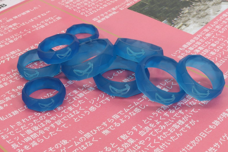 May include: A group of seven translucent blue rings with a geometric design. Each ring has a white design on the inside of the ring.