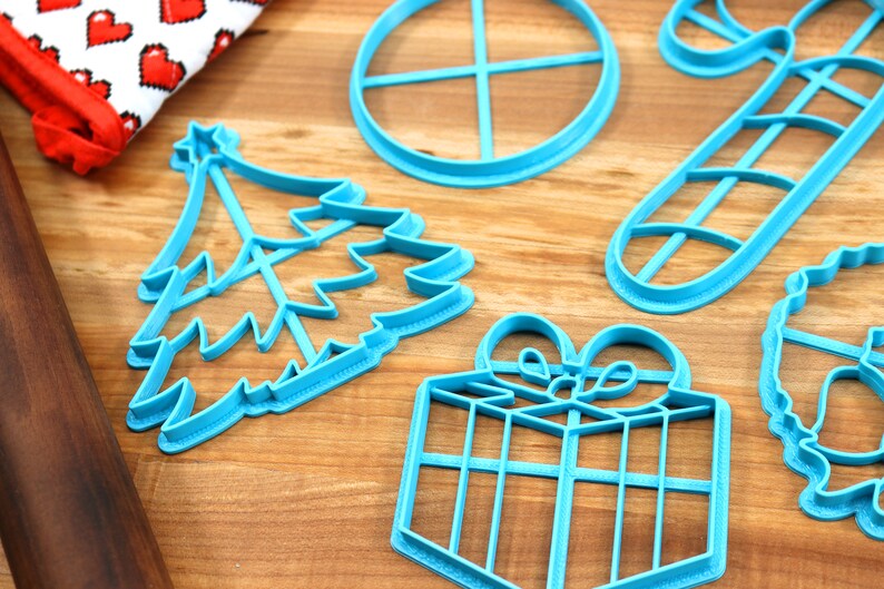 Op de afbeelding: Een set van zes blauwe plastic kerstkoekjesvormen. De vormen zijn in de vorm van een kerstboom, een snoepstok, een cadeau, een krans, een ster en een cirkel.