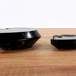 May include: Two black ceramic bowls with a gold flecked finish. The larger bowl is wider and shallower than the smaller bowl.