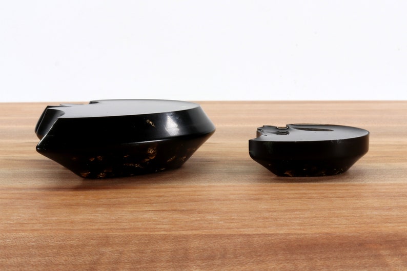 May include: Two black ceramic bowls with a gold flecked finish. The larger bowl is wider and shallower than the smaller bowl.