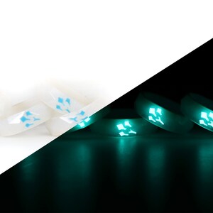 May include: A set of white silicone rings with a blue glow-in-the-dark design. The rings are shown in both daylight and dark conditions, highlighting their glow-in-the-dark feature.