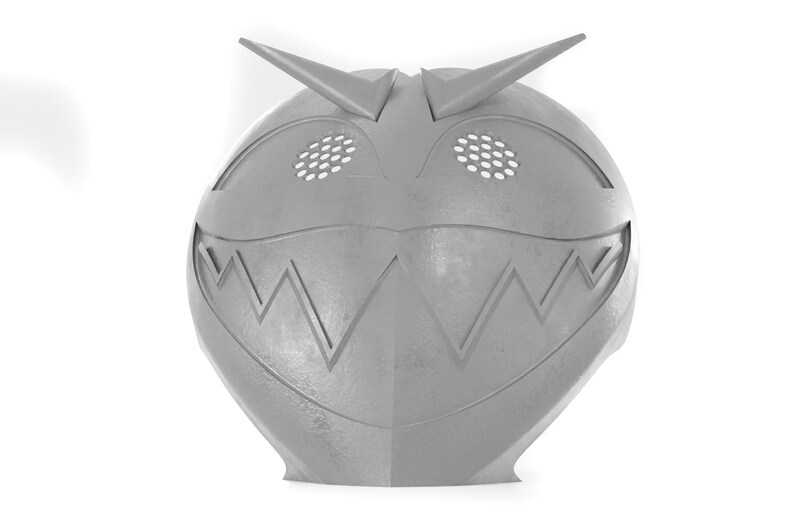 May include: A gray plastic mask with a toothy grin, sharp points on top, and two small holes for eyes.