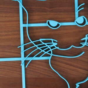May include: A blue 3D printed cat outline on a wooden surface. The cat's face is visible with eyes, whiskers, and a smile.
