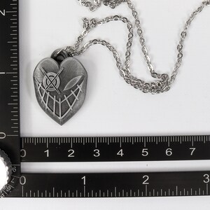 May include: A silver heart-shaped pendant necklace with a detailed design of a skull and crossbones. The necklace is on a silver chain.