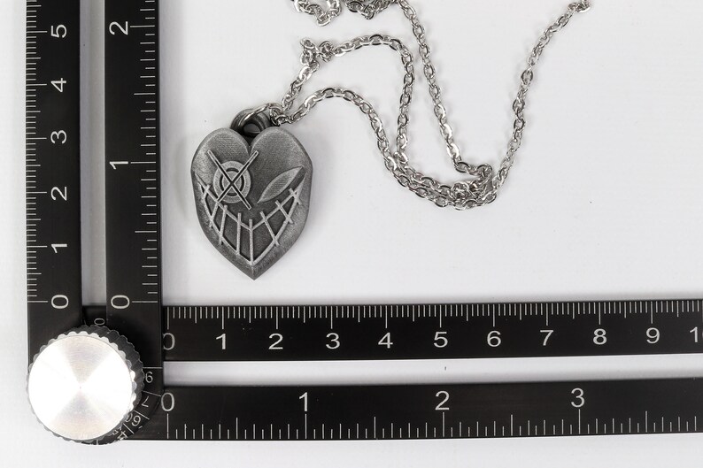 May include: A silver heart-shaped pendant necklace with a detailed design of a skull and crossbones. The necklace is on a silver chain.