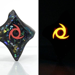 Pu&ograve; includere: Un ciondolo nero, iridescente, a forma di diamante con un motivo a stella rossa a tre punte. Il ciondolo brilla di arancione al buio.
