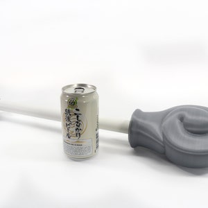 K&ouml;nnte beinhalten: Ein graues 3D-gedrucktes Objekt mit einem wei&szlig;en Stab und einer Dose japanischen Biers. Das Objekt hat ein abgerundetes Ende und ein zylindrisches Ende. Die Bierdose ist silber und beige mit japanischem Text.