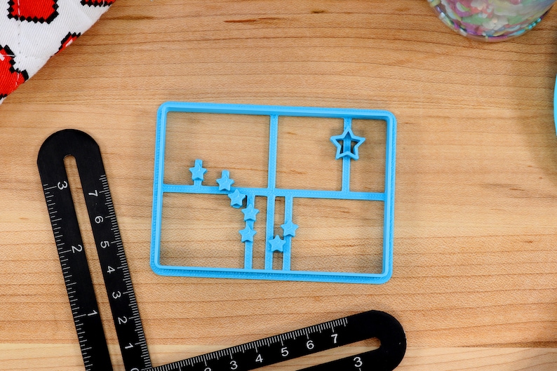 May include: A blue plastic cookie cutter shaped like a grid with nine star-shaped cutouts. The cookie cutter is on a wooden surface.