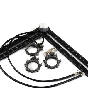 Puede incluir: Una cinta m&eacute;trica negra con un cord&oacute;n negro y tres anillos de metal plateado. La cinta tiene n&uacute;meros del 0 al 15.