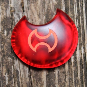 May include: A red crescent-shaped plastic token with a stylized yin-yang symbol in the center.