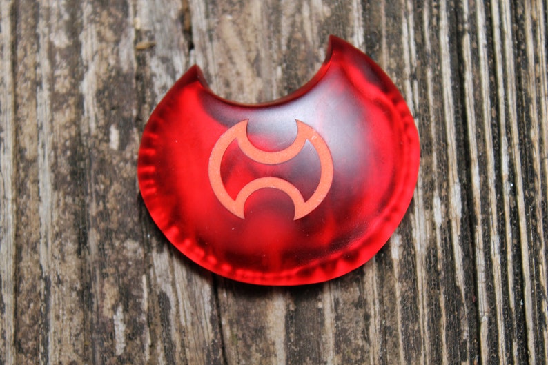 May include: A red crescent-shaped plastic token with a stylized yin-yang symbol in the center.