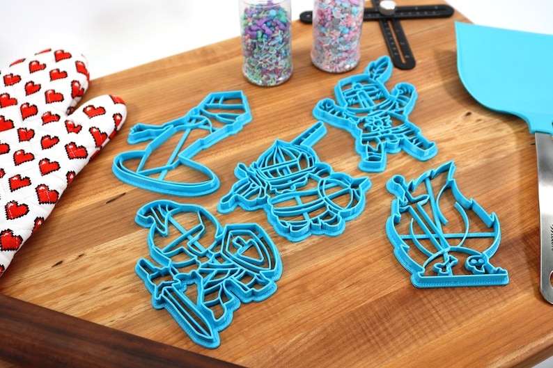 May include: A set of five blue plastic cookie cutters shaped like knights and a ship. The cutters are on a wooden surface.