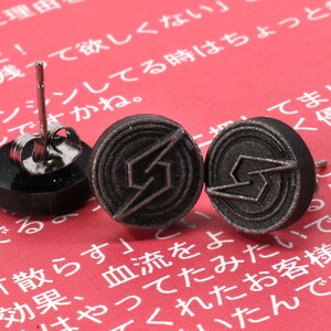 May include: Three black stud earrings with a silver lightning bolt design. The earrings are on a red background.