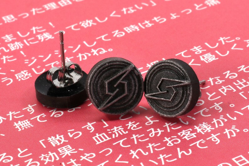 May include: Three black stud earrings with a silver lightning bolt design. The earrings are on a red background.