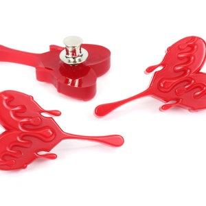 May include: Three red heart-shaped pins with a dripping effect. The pins have a silver metal backing.