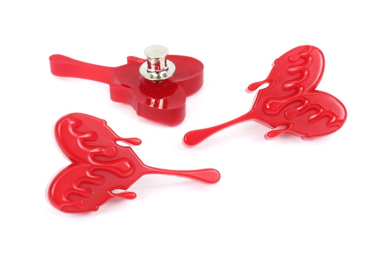 May include: Three red heart-shaped pins with a dripping effect. The pins have a silver metal backing.