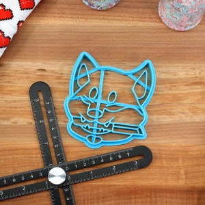 May include: A blue plastic cookie cutter shaped like a dog's head. The cutter has a detailed design with a smiling expression and a tongue sticking out.