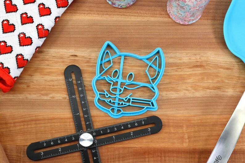 May include: A blue plastic cookie cutter shaped like a dog's head. The cutter has a detailed design with a smiling expression and a tongue sticking out.