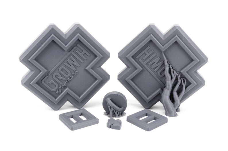May include: Two gray 3D printed plaques with the words "GROW WITH" and "HIM" on them. The plaques are shaped like a cross with a raised border. There are also three smaller gray 3D printed objects, including a basketball hoop, a small square, and a rectangle.