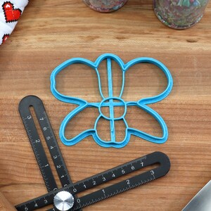 May include: A blue plastic flower-shaped cookie cutter on a wooden surface. The cutter has five petals and a center circle.