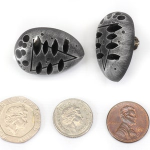 May include: Two silver-colored, oval-shaped earrings with a black, abstract design. The earrings are about the size of a US penny.