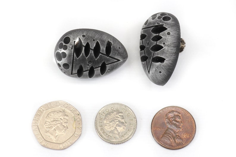 May include: Two silver-colored, oval-shaped earrings with a black, abstract design. The earrings are about the size of a US penny.