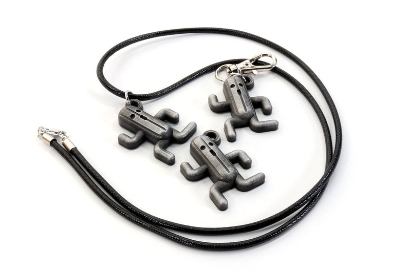 May include: Three silver-colored pendants shaped like stick figures with arms and legs, hanging from a black cord. The pendants are attached to a silver-colored clasp.