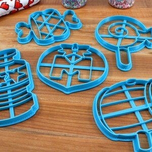 Puede incluir: Un juego de seis cortadores de galletas de pl&aacute;stico azul con forma de botella, barril, piruleta, &aacute;rbol de Navidad, hueso y gofre.