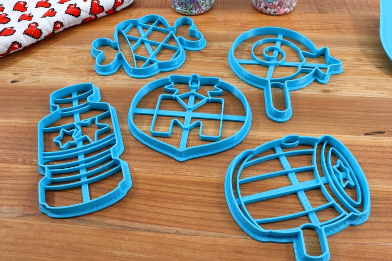 Puede incluir: Un juego de seis cortadores de galletas de pl&aacute;stico azul con forma de botella, barril, piruleta, &aacute;rbol de Navidad, hueso y gofre.