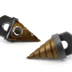 May include: Two metal drill bits with a gold and silver finish. One bit has a stepped, conical design, while the other has a flat, triangular shape. Both have a circular hole and a silver rivet.