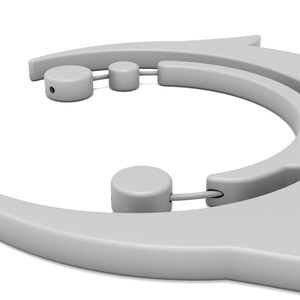 May include: A close-up of a light gray, plastic tool with a curved design. The tool has a series of rounded cylinders and a pointed end. The object is set against a white background.