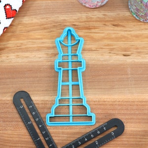 May include: A blue plastic cookie cutter shaped like a chess piece, a king. The cutter is on a wooden surface.