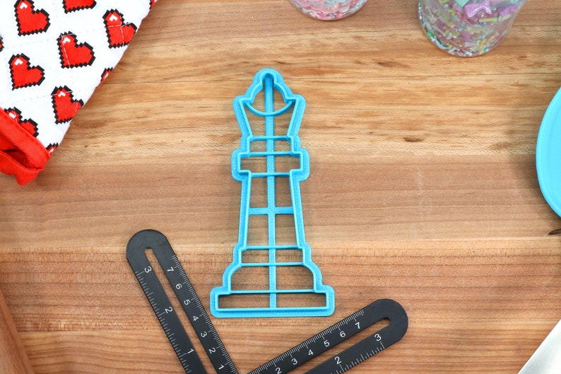 May include: A blue plastic cookie cutter shaped like a chess piece, a king. The cutter is on a wooden surface.