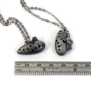 May include: Two silver ocarina necklaces with a ruler for size reference. The ocarinas are about 4 cm long.