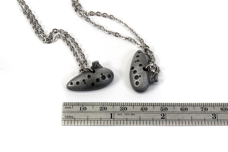 May include: Two silver ocarina necklaces with a ruler for size reference. The ocarinas are about 4 cm long.