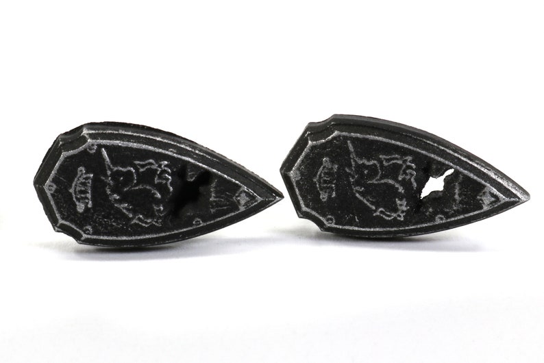 May include: Two black metal shields with a silver design of a unicorn and a crown. The shields are pointed at the top and have a rounded bottom.